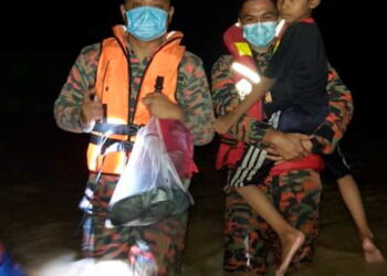 ANGGOTA bomba mendukung seorang kanak-kanak lelaki yang menjadi mangsa banjir di Kampung Batu 10, Skudai semalam.-ihsan Bomba Johor