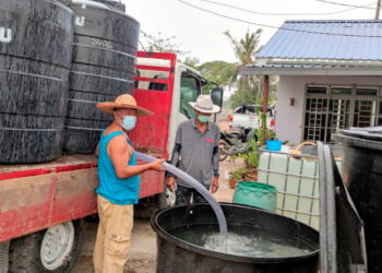 BOK Che Napiah (kiri) memasukkan air yang dihantar oleh SADA ke dalam sebuah tangki di Kampung Tengku Laksamana, Kuala Kedah semalam. -UTUSAN/MOHD ZAID MOHD NOOR