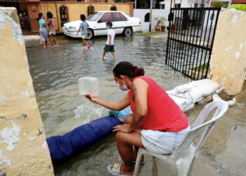 ELIZABETH Pereira menceduk air bertakung di halaman rumahnya apabila kawasan tersebut dinaiki air akibat fenomena air pasang besar di Perkampungan Portugis, Ujong Pasir, Melaka. - UTUSAN/RASUL AZLI SAMAD