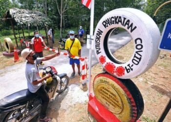 SAM Anak Chen (baju merah) memantau penduduk yang melalui pintu masuk di Kampung Orang Asli Jeram Kedah, Ulu Beranang, Lenggeng, Seremban. – UTUSAN/MOHD. SHAHJEHAN MAAMIN