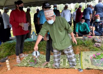 MOHD. Haris Helmi Hasbullah menyiram air di kubur bapanya selepas pengebumian di Tanah Perkuburan Islam Kampung Padang di Gerik hari ini. -UTUSAN/ ZULFACHRI ZULKIFLI