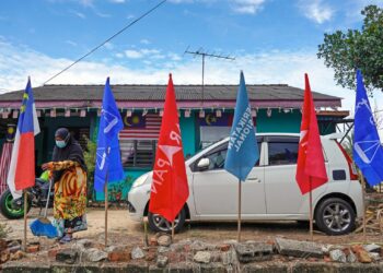 Suri rumah, Kamsiah Salim, 65, mengemas kawasan rumahnya yang dipasang beberapa bendera parti politik berbeza sempena Pilihan Raya Negeri Melaka pada 17 November 2021. -UTUSAN/AMIR KHALID