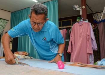 KAMARUDIN Mustafar menyiapkan tempahan baju Melayu pelanggan bagi sambutan Aidilfitri di Kampung Pinang Merah, Dungun, Terengganu. - UTUSAN/PUQTRA HAIRRY ROSLI