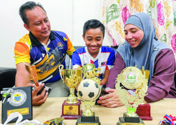 UZZAIR ZAYYAN (tengah) yang bakal masuk ke Akademi Cruzeiro, Brazil bersama ibu dan bapanya melihat koleksi piala yang dimenangi di rumah mereka di Kampung Tunjong, Beseri, Perlis semalam.- UTUSAN/NAZLINA NADZARI