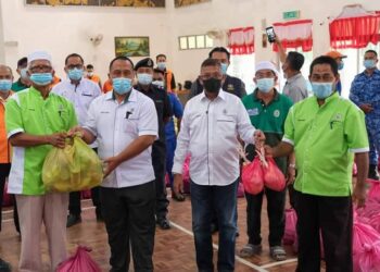 HANAFIAH Mat (dua dari kanan) menyerahkan barangan keperluan makanan kepada wakil penduduk di Mukim Rasau, Dungun di Terengganu hari ini.