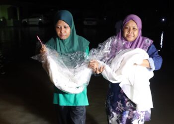 NORHAZILAH Moin (kiri) bersama kakaknya, Norhanidah mengangkat baju pernikahan yang sempat diselamatkannya dalam kejadian banjir di Kampung Kilang Berapi, Merlimau di Jasin. UTUSAN/ RASUL AZLI SAMAD