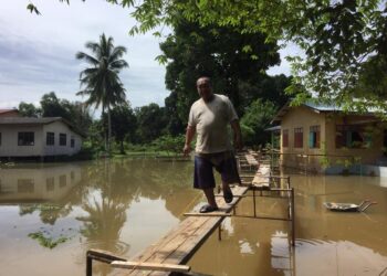 MOHD. Rosdi Abdullah berjalan di atas titi yang dibina bagi mengelak mengharungi banjir di Kampung Lubok Gong, Rantau Panjang, Kelantan. - UTUSAN/YATIMIN ABDULLAH