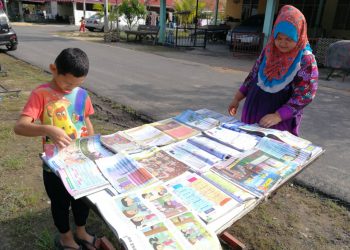 FARALIZA Che Hussin, 35, dan anaknya, Mohd. Syaq Fayat menjemur buku teks di hadapan rumah mereka di Rumah Mampu Milik (RMM) Telok Kalong di Kemaman hari ini. -UTUSAN/Nik Nur Izzatul Hazwani Nik Adnan