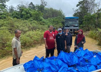 MUHAMAD Yusrizal Ghani (tengah) bersama bakul makanan yang diagihkan kepada mangsa banjir Orang Asli di Kampung Pasir Linggi, Gua Musang, Kelantan.