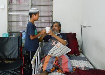 MUHAMMAD Mu’az Zhofri Mohamad Yong (kiri) membantu menguruskan bapanya, Mohamad Yong Awang yang kabur penglihatan dan tidak boleh berjalan di Kampung Losong Haji Mat Shafie di Kuala Terengganu, semalam.