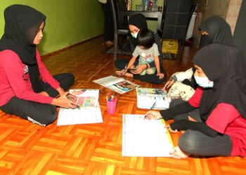 ANNUR Fakhira Mohd. Abdullah (dua dari kiri) meriba salah seorang adiknya sambil menggunakan telefon pintar ibu mereka bagi mengikuti PdPR bersama adik-beradik lain di PPR Melana Indah, Tampoi, Johor.