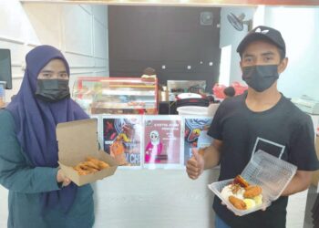 MOHAMMAD Atif Wan Kamal (kanan) dan isterinya, Siti Nazirah Norzri menunjukkan nasi lemak ayam goreng yang diberikan percuma kepada golongan memerlukan di kedai mereka, Ateyh Fried Chicken di Taman Nong Chik, Johor Bahru, Johor. -UTUSAN/KHAIRUL MOHD ALI