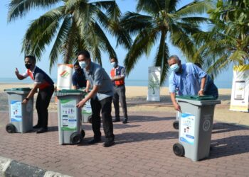 TEO Kok Seong (tengah ) menampal pelekat maklumat KITARecycle pada tong samlah beroda di Pantai Saujana, Batu 4, Port Dickson hari ini.-UTUSAN/ZAKKINA WATI AHMAD TARMIZI.