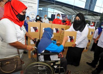 NAJWA Halimah Ab. Alim (kanan) menyampaikan sumbangan kepada Ing@Taibah Abdullah yang merupakan pemandu teksi yang berkerusi roda sempena Majlis Program Prihatin Bersama Pemandu Teksi di Terminal Feri Puteri Harbour, Johor. -UTUSAN/RAJA JAAFAR ALI