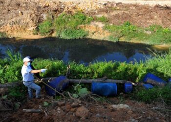 HASNI Mohammad (kiri) melihat beberapa tong biru yang ditemukan di tebing sungai ketika menyelusuri denai Sungai Kim Kim sepanjang dua kilometer di Pasir Gudang, Johor. -UTUSAN/ RAJA JAAFAR ALI