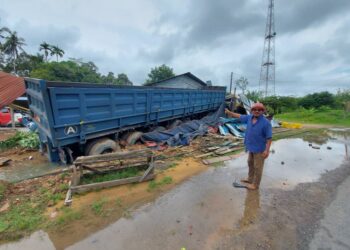 MOHD. Noor Jusoh menunjukkan lori treler muatan bijih besi yang terbabas dan melanggar kedai makan di Kampung Seboy Kuala Krau, Pahang.