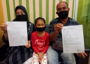 ROSLI Md. Salleh (kanan) dan Zarinawati Zainal Abidin menunjukkan salinan laporan polis berkenaan anak angkat mereka, Chinta Tiara Leona (tengah) ketika ditemui di Felda Chemplak, Labis di Johor. -UTUSAN/FARAHWAHIDA AHMAD