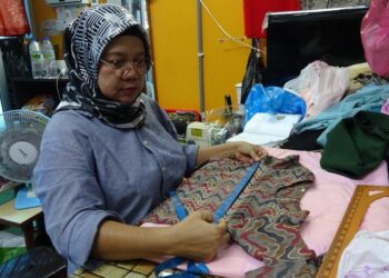 ROSHAYATI Ahmad tetap gigih meneruskan aktiviti menjahit walaupun berdepan kemerosotan tempahan baju raya tahun ini di Pasar Besar Kuantan di Kuantan, Pahang. - UTUSAN/DIANA SURYA ABD. WAHAB