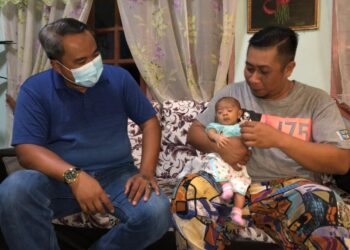 SHAHRIZAN Yusof (kanan) memangku anak bongsunya, Qish Naura Syifa yang akan menjalani pembedahan jantung berlubang ketika dikunjungi Mohd. Fadel Alwi di Kampung Sri Lalang, Kluang, Johor. -UTUSAN/NUR NABILAH RAHMAT