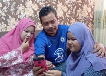 MOHD Izzuddin (tengah) dan Norfadila (kiri) melihat keputusan SPM Norizatul Izzlyn di skrin telefon pintar di rumah mereka di Kampung Bukit Changgang Banting. -UTUSAN/ABDUL RAZAK IDRIS