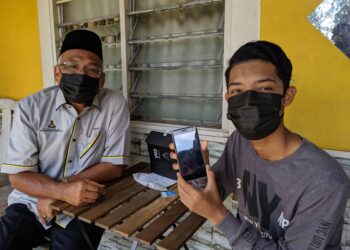 MUHAMMAD Asmadi Ahmad Zabidi menunjukkan telefon pintar jenama YES sumbangan kerajaan negeri yang diterimanya. - UTUSAN/MOHAMAD HAFIZI MOHD. SAID