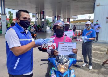 MOHD. Hairi Mad Shah (kiri) mengedarkan bungkusan KFC selepas mengisi minyak secara percuma kepada penunggang motosikal anjuran Pemuda UMNO Johor di Taman Pelangi, Johor Bahru di Johor. - UTUSAN/KHAIRUL MOHD ALI