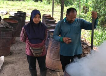 PASANGAN suami isteri, Azman Tamilselvan Abdullah dan Aisyah Chang menjana pendapatan dengan menghasilkan arang daripada tempurung kelapa terbuang di Kampung Kundur, Gua Musang. - UTUSAN/AIMUNI TUAN LAH