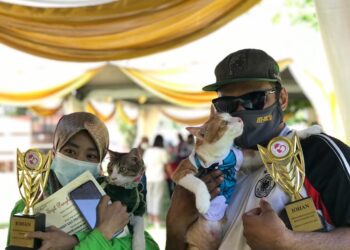 MOHAMED Shahrizzal Mohamed Tajuddin (kanan) mendukung kucingnya, Boy yang menang pertandingan Kucing Kurang Upaya dan Kucing Makan Paling Laju manakala isterinya, Nur Fadzilah Jamri mendukung kucing bernama Jendoi yang menang pertandingan Kucing Paling Berhias dalam Festival Kucing Jalanan di Gopeng hari ini. - UTUSAN/LIYANA RAMLI