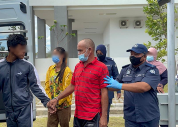 MAHMUD SULAIMAN (baju merah) dibawa keluar dari pekarangan Kompleks Mahkamah Kangar selepas dihadapkan ke Mahkamah Sesyen atas tuduhan menyeludup pendatang asing tanpa izin (PATI) di Kangar, Perlis hari ini. - UTUSAN/ NAZLINA NADZARI