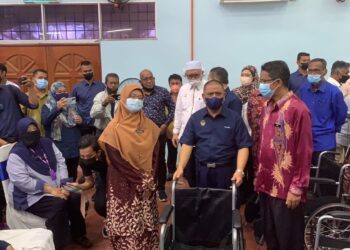 SAARANI Mohamad (tengah) menyerahkan kerusi roda pada pogram CSR di Bota Kanan dekat Parit hari ini. - UTUSAN/MOHAMAD HAFIZI MOHD SAID