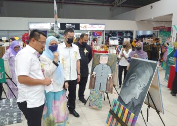 MOHD. Hairi Mad Shah (kiri) mendengar penerangan berhubung seni lukisan yang dihasilkan sempena Fiesta Seni Mini Johor di Paragon Market Place, Johor Bahru.