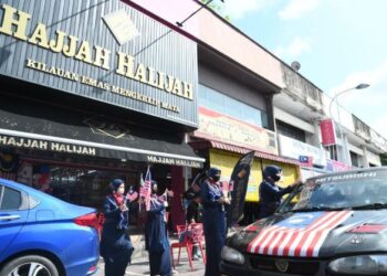 KAKITANGAN kedai emas Hajjah Halijah mengedarkan Jalur Gemilang kepada kenderaan yang melalui  sekitar kawasan kedai emas tersebut di Kangar, Perlis, baru-baru ini. –  UTUSAN/IZLIZAN OTHMAN.