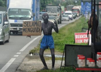 PENIAGA itik salai, Ikmal Hakim, 21, dengan kostum Spiderman memegang kepingan kotak tertera 'Selamat Mengundi' bagi menarik perhatian pengguna jalan raya di Jalan Seremban-Kuala Pilah dekat Terachi, Kuala Pilah. - UTUSAN/MOHD SHAHJEHAN MAAMIN