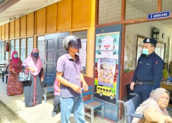 POLIS memujuk seorang lelaki OKU yang enggan membuka topi keledar yang dipakai semasa membuang undi di SK Padang Mandol, Tumpat, Kelantan.-UTUSAN/ROHANA ISMAIL.