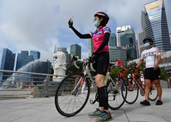 SEORANG penunggang basikal mengambil gambar berhampiran patung singa Merlion di Singapura. - AFP