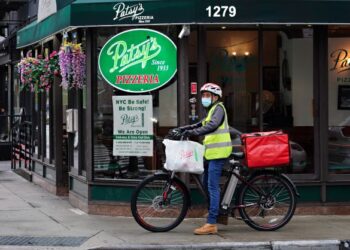 PEKERJA penghantaran makanan berhenti di hadapan kedai Patsy's Pizzeria di New York.-AFP