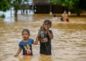 ADAM Zafriel Hamizi dan Hanifa Khaira Mohd. Khairul Radzi meredah air sambil membawa monyet peliharaan mereka di Kampung Kubang Betong, Changlun, Kedah yang dilanda banjir, semalam. – UTUSAN/ SHAHIR NOORDIN