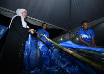 ROZIEANA Ahmad memeriksa bendera bersama petugas sebelum ia dibawa ke kawasan-kawasan pemasangan yang strategik di sekitar Jelempok, Guar Sanji, Arau Perlis.- UTUSAN/IZLIZAN OTHMAN