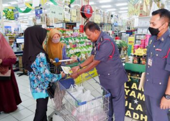 A. RAVI (tengah) menyampaikan risalah berkaitan keselamatan kebakaran kepada pelanggan di pasar raya TF Value Mart Tapah hari ini. - UTUSAN