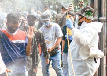 PETUGAS perubatan menyembur cecair pembasmi kuman terhadap orang ramai yang beratur untuk mengambil suntikan vaksin Covid-19 di Bandung, Indonesia. - AFP