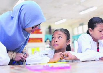 SEORANG guru bertanyakan sesuatu kepada seorang murid yang sedang menyiapkan kerja sekolah. SOP akibat Covid-19 makin membebankan tugas guru ditambah pula dengan isu huru yang sudah bersara tidak diganti. - FOTO HIASAN