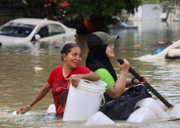 PENDUDUK cuba mengharungi banjir bagi menyelamatkan diri selepas kawasan kediaman mereka di Taman Sri Muda ditenggelami air. - FOTO/ZULFADHLI ZAKI