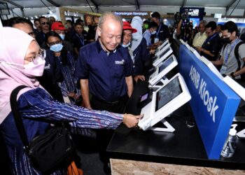 Arifin Zakaria melihat salah seorang pengunjung, Noor Syahidah Ramlee, 34, mengemas kini butiran peribadi di kiosk ASNB di tapak pameran MSAM 2022 di Port Dickson, hari ini.-UTUSAN/MOHD SHAHJEHAN MAAMIN.