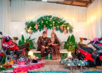 PASANGAN pengantin, Nurul Alwani Khalda dan suami, Ahmad Muzzammil Samsudin bergambar di pelamin bersama hantaran termasuk motosikal Yamaha RXZ dan NVX yang tular dalam media sosial. – HAZRUL FOTO II MOMENTO