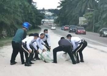 BEBERAPA anggota trafik IPD Kulai membantu mengalihkan guni pasir ke bahu jalan dalam kejadian yang berlaku di Jalan Kulai-Johor Bahru semalam. - FACEBOOK PDRM