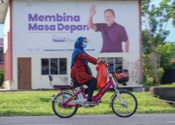 Seorang wanita melepasi poster Menteri Besar, Datuk Seri Ir. Hasni Mohammad di Benut, Johor, semalam. UTUSAN/FARIZ RUSADIO