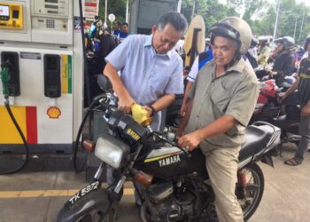 AHMAD Razif Abd. Rahman membantu seorang penunggang motosikal mengisi minyak pada program isi minyak percuma di sebuah stesen minyak di Kampung Teluk Ketapang, Kuala Nerus, Terengganu, hari ini.  - UTUSAN/TENGKU DANISH BAHRI TENGKU YUSOFF