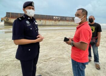 MOHAMAD Ismail Jamaluddin (kiri) bersama M. Fakrul Razzi Muhammad ketika meninjau tongkang yang tersadai di Pantai Melawi, Bachok, hari ini. - FOTO/TOREK SULONG