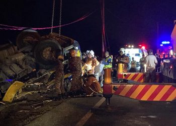 ANGGOTA bomba mengeluarkan mangsa daripada treler muatan simen yang terbalik di Jalan Lama Kota Bharu, Gopeng, Perak, malam tadi. - GAMBAR IHSAN JBPM