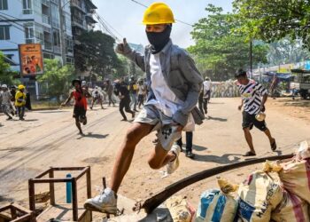 SEORANG penunjuk perasaan melompat melepasi hadangan yang dibuat dalam tunjuk perasaan di pekan Thaketa, Yangon, Myanmar. - AFP